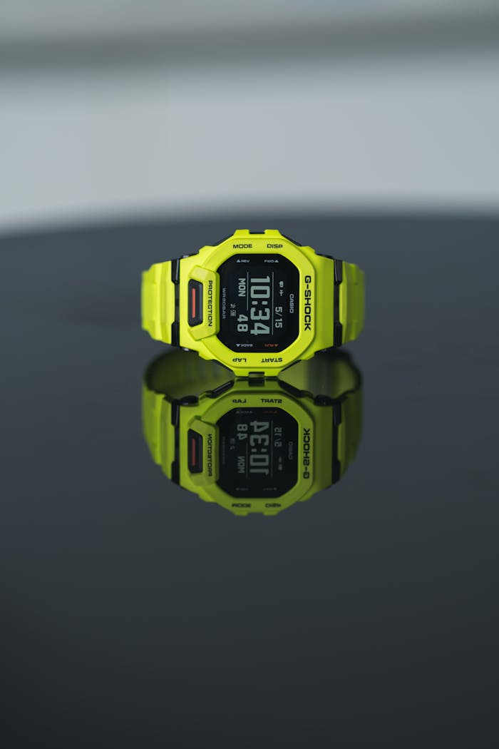 A vibrant yellow digital watch displayed on a glossy black surface, showing time clearly.